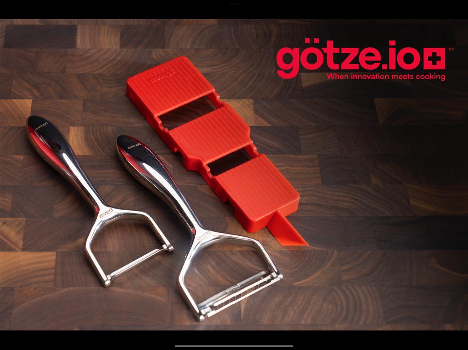 Götze Luxury Premium Peeler with a red handheld slicer displayed on a dark wooden cutting board.