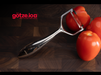 Götze Luxury Premium Peeler removing thin skin from a fresh tomato on a dark wooden cutting board.
