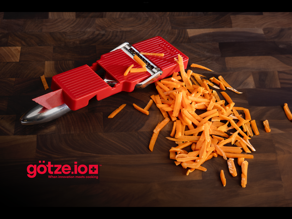 Götze Luxury Premium Peeler cutting fresh carrots into thin matchstick strips on a dark wooden cutting board.