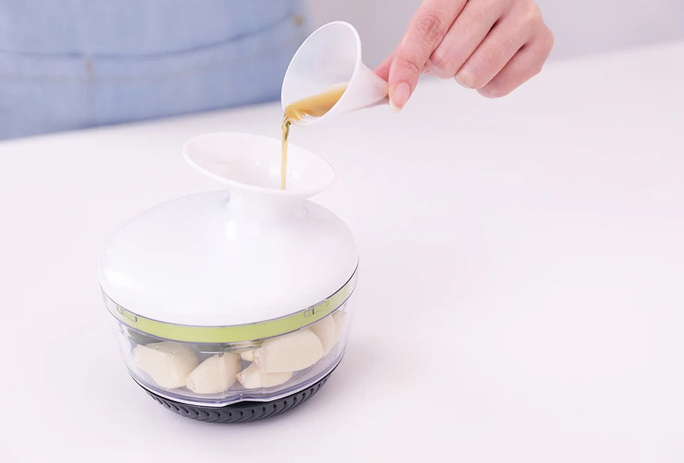 Götze Mavo manual food chopper with garlic cloves inside while liquid is poured through the top opening of the white lid.