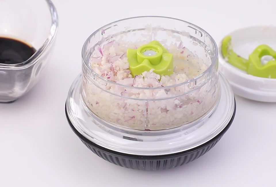 Götze Mavo manual food chopper filled with finely chopped red onion, featuring a clear container, green blade system, and black non-slip base.