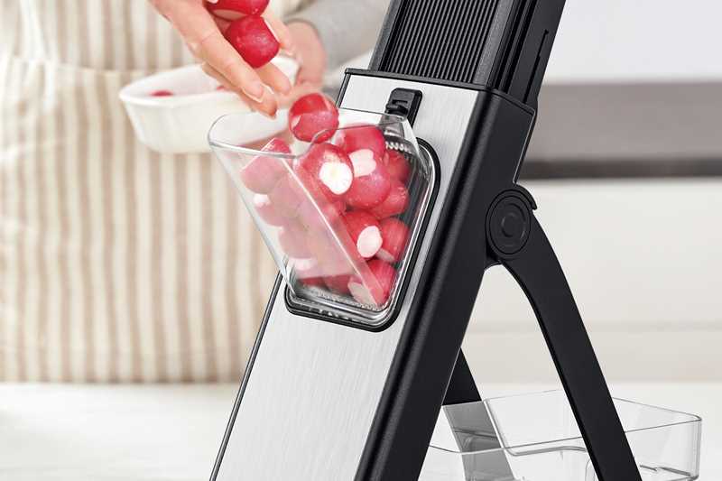 Götze SafeSlice Pro mandoline slicer in use with fresh radishes loaded into the safety food holder and sliced into the clear collection container.