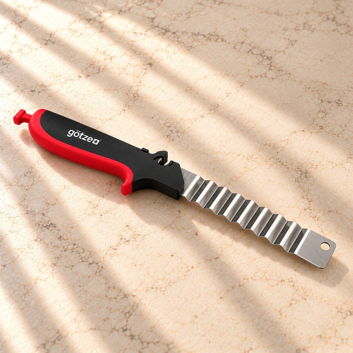 Götze wavy blade with a red and black handle on a marble countertop in warm sunlight