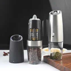 Electric pepper and salt grinder shown with battery compartment open, clear spice chamber, black and stainless steel body, and a second assembled grinder beside it.