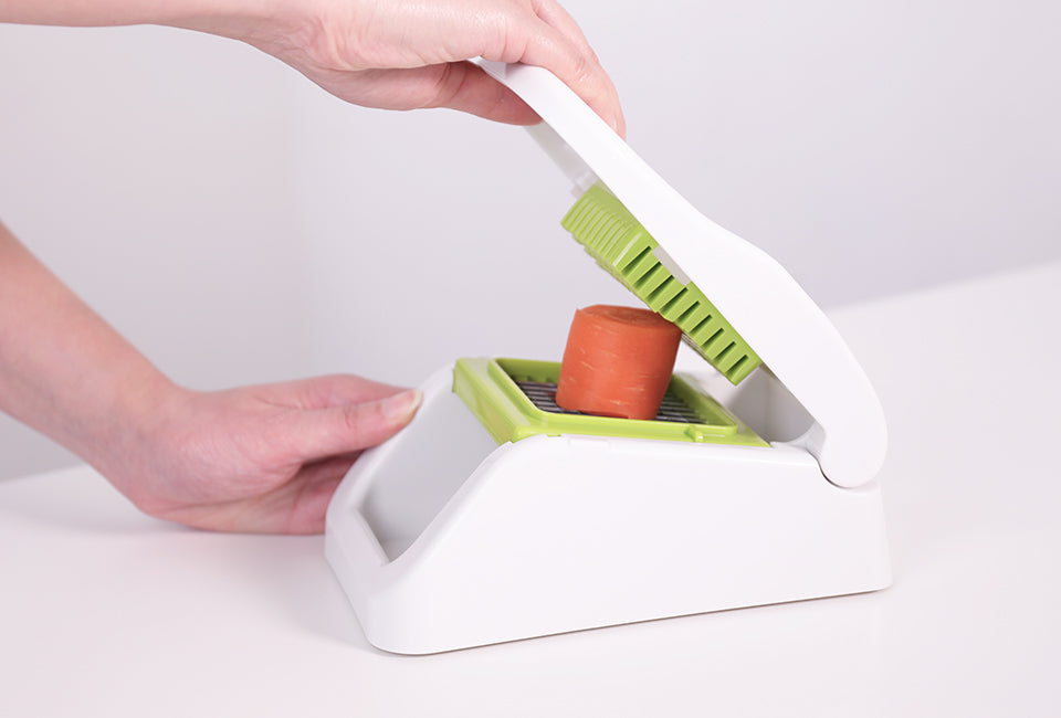 Götze FreshCut Food Dicer being used to press a carrot through the green stainless steel cutting grid for quick, even dicing.
