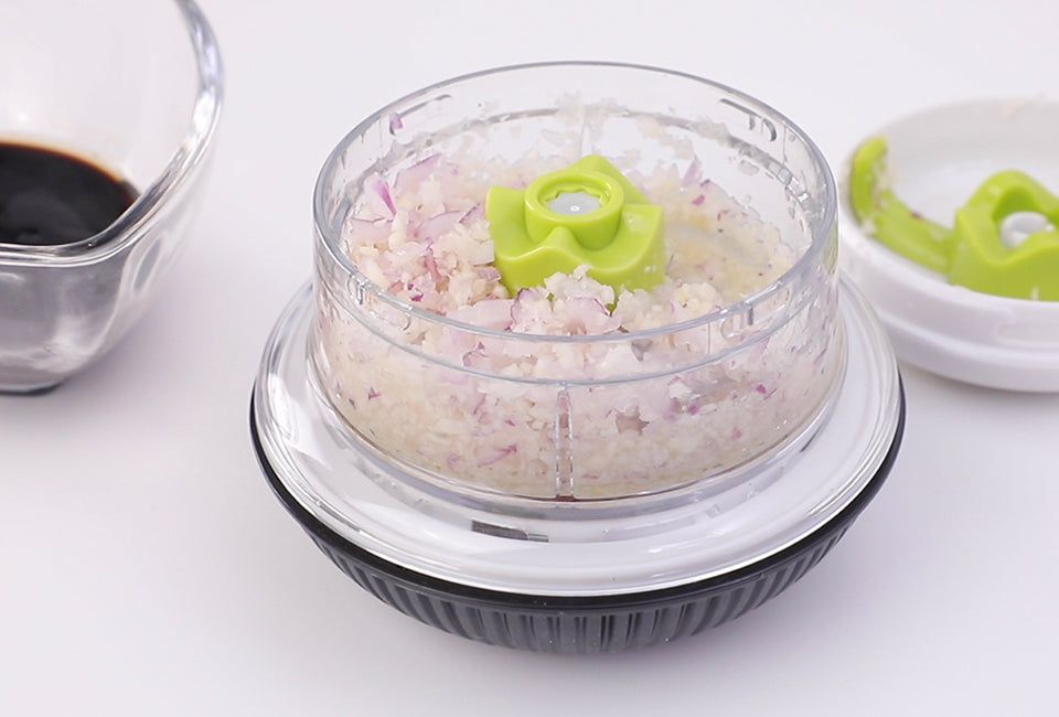 Götze Mini Mavo manual food chopper filled with finely chopped red onion, featuring a clear container, green blade system, and black non-slip base.