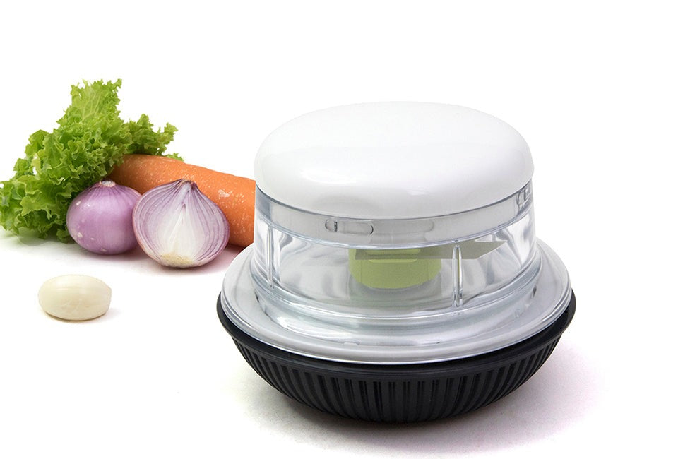 Götze Mini Mavo manual food chopper with clear container, white lid, green blade system, and black non-slip base displayed with lettuce, carrot, red onion, and garlic.
