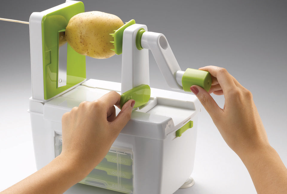 Götze Premium Vegetable Spiralizer being used with a potato, featuring a hand crank, secure food holder, slicing blade, and built-in storage base.
