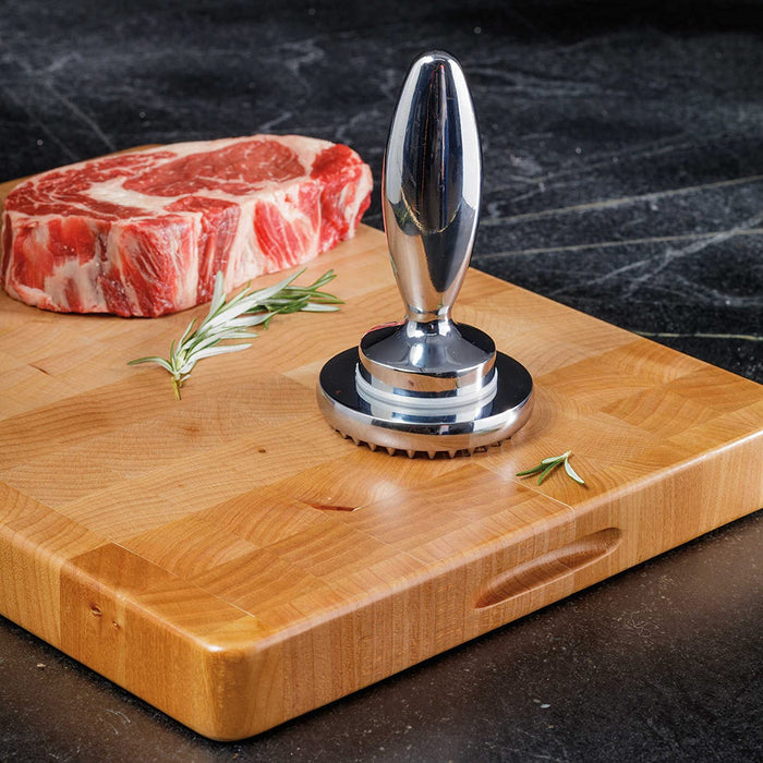 Götze Reversible Dual-Sided Meat Tenderizer & Pounder displayed on a wooden cutting board beside a raw steak and fresh rosemary.