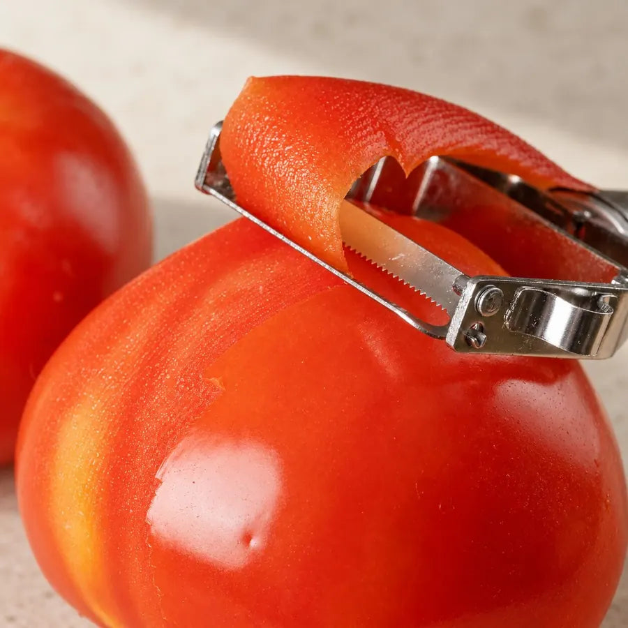 Götze stainless steel peeler removing the skin of a ripe red tomato
